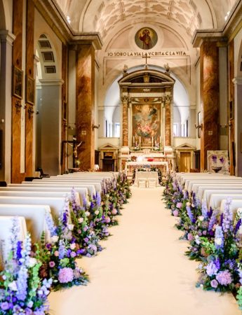 In quella foto la navata di una chiesa allestita con fiori dai toni del rosa e del glicine