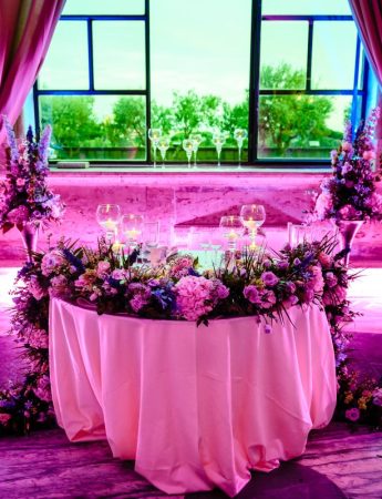 In questa foto un raffinato tavolo degli sposi arricchito con fiori rosa e glicine